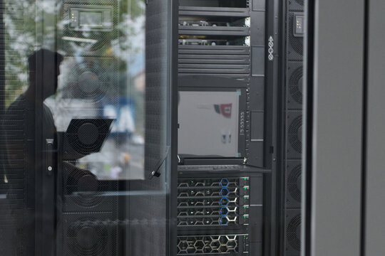 Data center server racks and monitoring equipment reflected in glass with technician working in modern facility