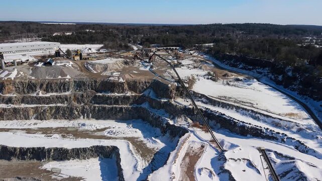 Aerial view of a quarry, where the stark white of snow contrasts with the exposed rock and machinery amidst a forest backdrop, Plainville, Massachusetts, United States.
