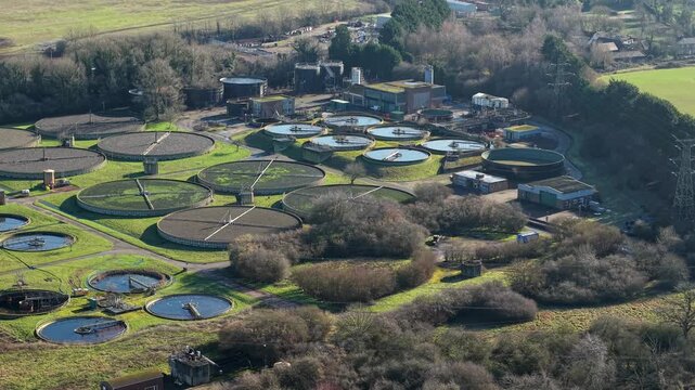 Aerial view of a water treatment plant with circular tanks surrounded by lush greenery and buildings, Luton, England, United Kingdom.