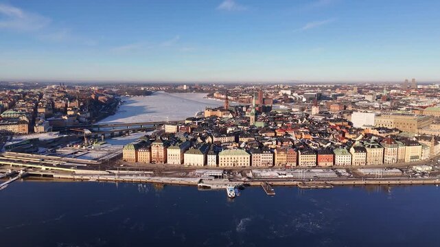 Aerial view of buildings along the water's edge with a bridge in the distance, contrasting with the clear blue sky, Stockholm, Stockholm County, Sweden.