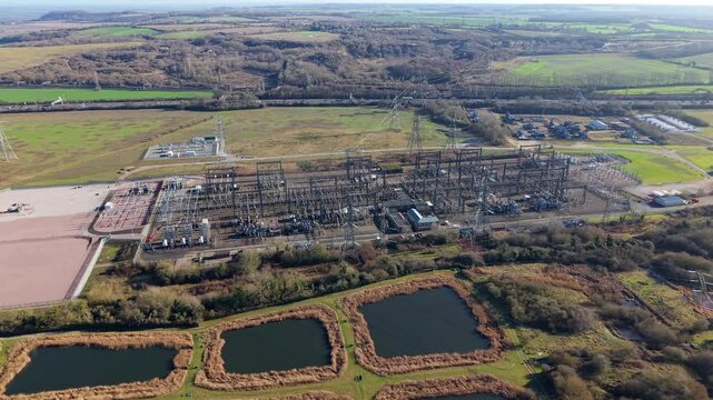 Aerial view of an electricity substation surrounded by autumn colors of fields and trees, contrasting with the metallic structures, Luton, England, United Kingdom.