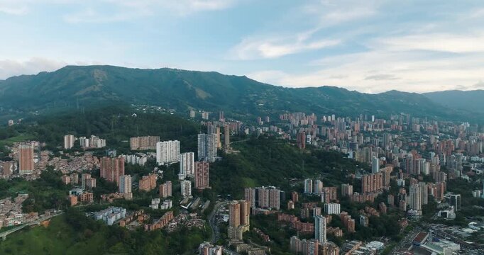 Aerial view of buildings of varying heights nestled against green mountains under a cloudy sky, creating a striking contrast, Medellin, Antioquia, Colombia.