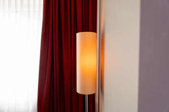 Leuchtende Stehlampe im Hotelzimmer vor Fenster und roten Vorh&auml;ngen.