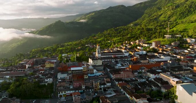 Aerial view of closely packed buildings nestled amidst lush green mountains and valleys, a vibrant tapestry of urban and natural landscapes, Tamesis, Antioquia, Colombia.