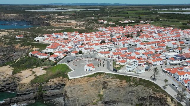 Aerial view of Zambujeira do Mar village with its white houses and red roofs, perched on cliffs above the ocean, Zambujeira do Mar, Beja District, Portugal.