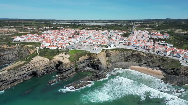 Aerial view of the village of Zambujeira do Mar perched atop rugged cliffs where white-washed buildings meet the turquoise ocean, Zambujeira do Mar, Beja District, Portugal.