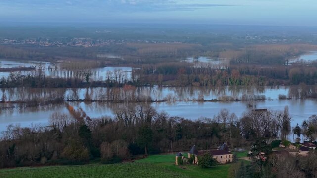 Aerial view of the serene river reflecting the sky's pale hue, entwined with islands of trees, and a small village nestled in the foreground, Paillet, Nouvelle-Aquitaine, France.