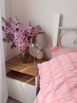 A bouquet of lilacs in a vase near a bed with pink bedding, coquette morning with flowers, morning bedroom 
