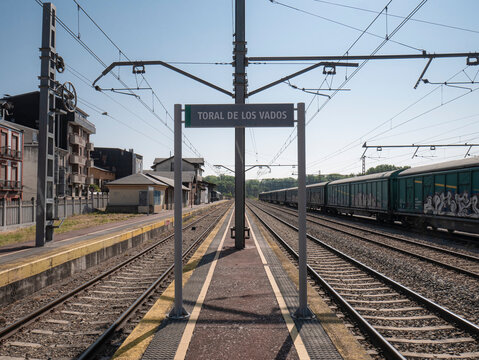Toral de los Vados, Leon, Spain, 06-16-2025: Sign with the name of the train station located on a platform and the station's passenger building completely empty early in the morning
