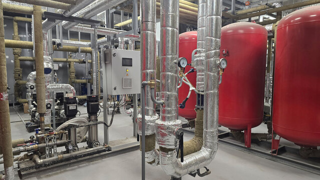 Interior view of industrial facility displaying red pressure tanks alongside metallic piping systems equipped with valves and gauges, highlighting sophisticated arrangement of machinery and equipment