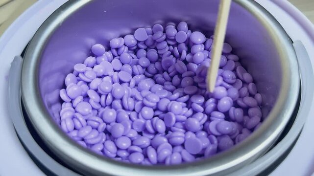Purple hard wax beads filling a professional wax heater, providing a convenient and effective solution for body hair removal and smooth skin in a beauty salon or spa setting