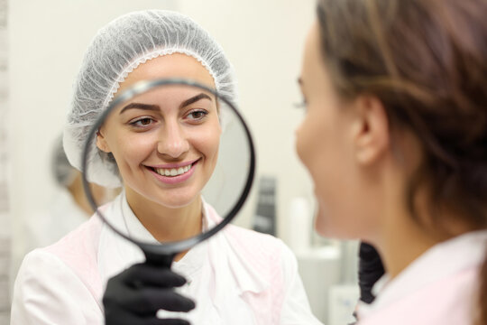 close-up of female client examining her skin in mirror after blackhead mask removal, beautician smiling beside her, bright salon interior