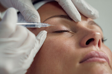 Naklejka premium close-up of model receiving facial filler injection from experienced cosmetologist, medical gloves, clean clinical environment, soft diffused lighting