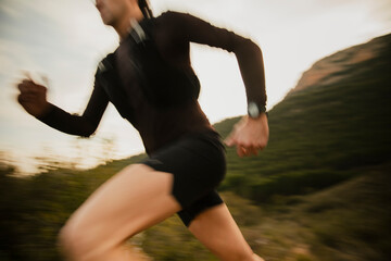 Dynamic motion blur photograph of a trail runner sprinting along a mountain trail during outdoor endurance training. Speed and action captured in natural landscape. © aitor