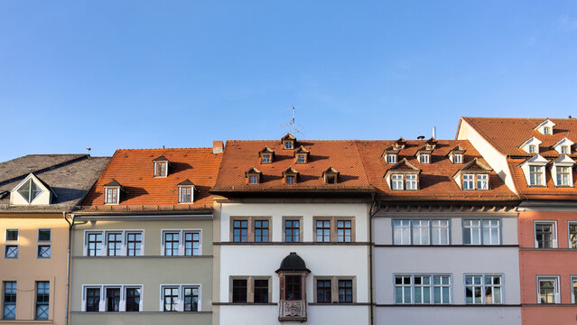 Historische H&auml;userzeile in Weimar mit typischen Fassaden und roten D&auml;chern unter blauem Himmel.