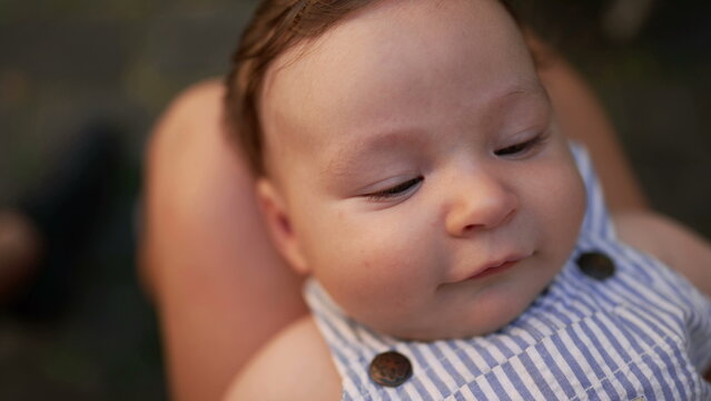 Close-up of baby resting on mother&rsquo;s lap with gentle smile and relaxed expression, outdoor setting, intimate family bonding, soft facial features in focus