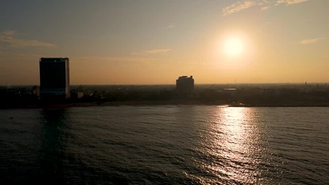 4K glowing morning sun rising above a hazy beach town and calm sea at dawn