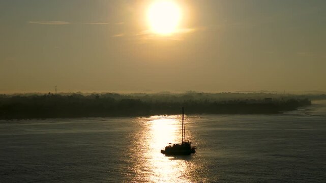 4K aerial view of a sailboat floating on calm ocean water during a golden hazy sunrise