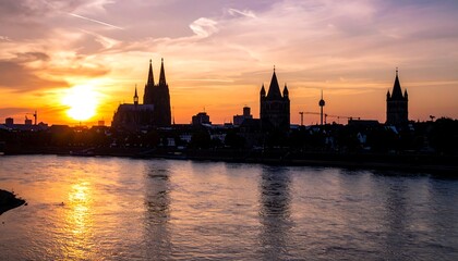 Fototapeta premium City skyline silhouette over a river, bathed in golden sunset light with purple hues and bright sunburst