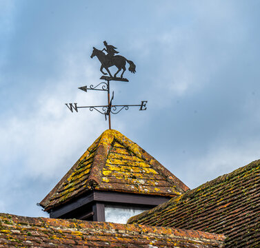 A weathered vane atop an old tiled mossy roof.