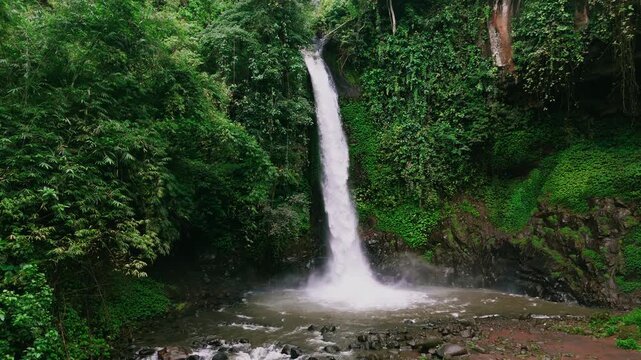 Aerial drone view of a high waterfall cascading into a pool in a lush tropical forest in East Java, Indonesia