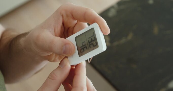 Close-up of a hand holding a digital thermometer and hygrometer, checking indoor temperature and humidity levels to prevent mold growth and maintain a healthy home environment.
