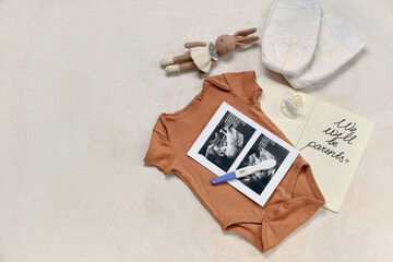 Baby clothes, sonogram images, pregnancy test and notebook with text WE WILL BE PARENTS on grunge beige background