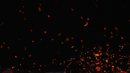 Floating orange sparks and embers rising in the dark, creating an abstract fire texture with copy space for energy, heat, welding, and night combustion concepts. © kinomaster
