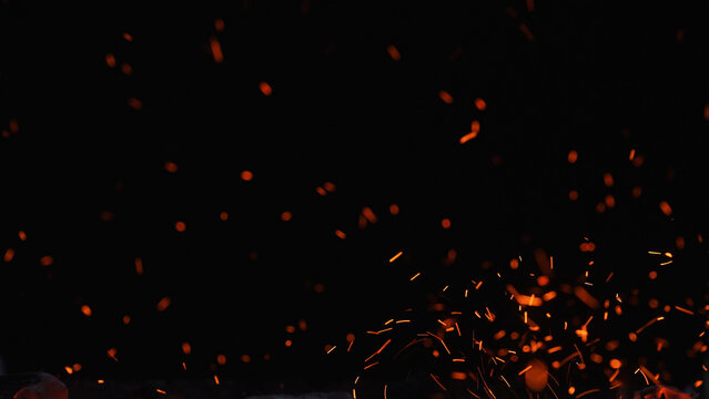 Floating orange sparks and embers rising in the dark, creating an abstract fire texture with copy space for energy, heat, welding, and night combustion concepts.
