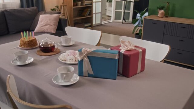 No people zoom in shot of festive table set with cake, teapot and cups, marshmallows on plate, blue and pink gift boxes tied with ribbons