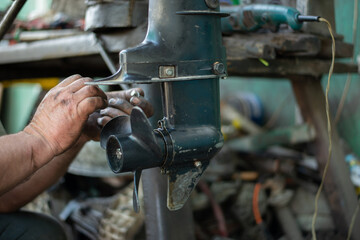 The hands of a master auto mechanic repair a gasoline outboard marine engine. The mechanic's hands are stained with oil and salidol. In the frame is the propeller and pump of the boat unit © Rystemys