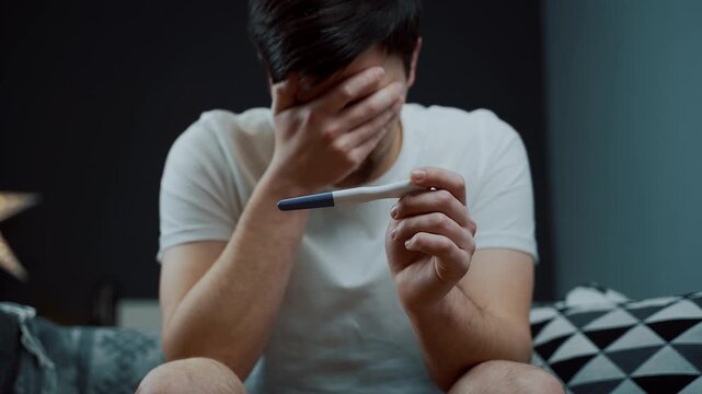 Portrait of man in deep despair clutching pregnancy test. Captures moment of intense emotional breakdown and mental exhaustion regarding family news. Shocked man looking at pregnancy test. 