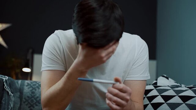 Mans hands trembling while holding a pregnancy stick. Highlighting the emotional vulnerability and stress men face during reproductive uncertainty. Man in deep despair clutching a pregnancy test.
