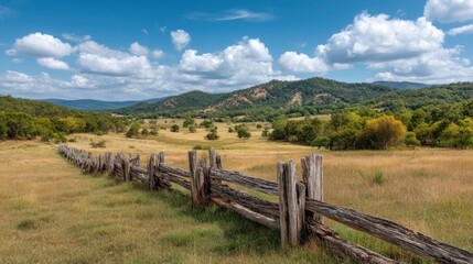 Scenic Landscape with Rolling Hills, Rustic Fence, Green Meadow, and Expansive Blue Skies Under Fluffy White Clouds
