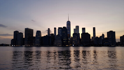 Obraz premium Silhouette of New York City Skyline at Dusk with Iconic Skyscrapers Reflected in Water, Urban Landscape Photography for Travel and Business Backgrounds