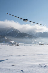 Fototapeta premium Sleek Glider Soaring Gracefully over Snow-Covered Mountains and Frozen Landscape under Clear Blue Sky with Wispy Clouds