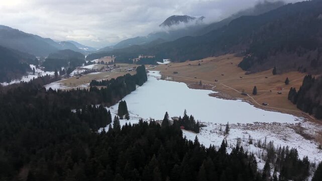 High altitude aerial view of Wagenbruchsee in Kruen, Germany. The snowy lake is surrounded by the Karwendel mountains. A top-rated tourist spot in the Garmisch-Partenkirchen area.