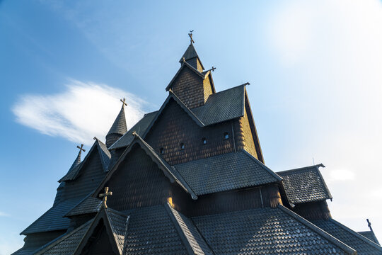 View of a dark, imposing Heddal stave church rises dramatically against a bright blue sky, its intricate wooden architecture a testament to history, Heddal, Telemark, Norway.