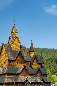 View of a towering wooden Heddal Stave church with intricate carvings and steeply pitched roofs reaching towards a clear blue sky, Heddal, Telemark, Norway.