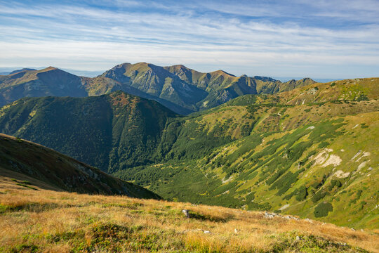 View of sun-kissed mountains with shades of green and brown under a blue sky, a serene landscape, Liptovske Kopy, Presov Region, Slovakia.