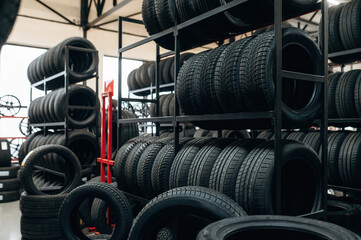 Stacked black rubber tires on metal shelves inside a tire shop with additional tires on the floor...