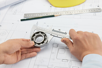 Engineer Measuring Ball Bearing with Calipers on Blueprint