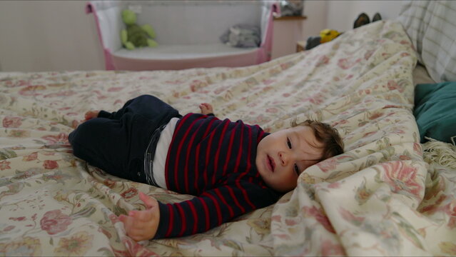 Baby lying on bed complaining with arms outstretched, seeking attention and comfort, early signs of fussiness in cozy family bedroom with soft bedding and natural light