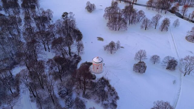 Panoramic winter view of Munich landmarks. Drone footage of the Englischer Garten at sunrise, featuring the Monopteros with the iconic towers of the historic center visible in the distance