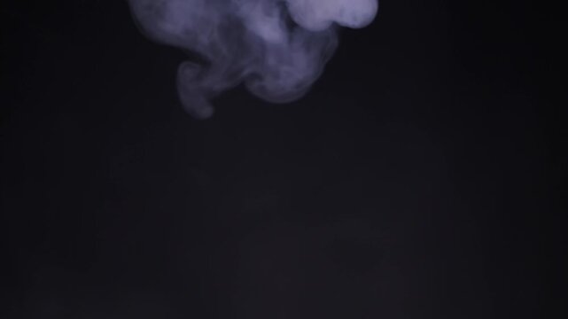 Dense white smoke pours from the top of the frame and swirls down against a  black background. Concept of mystery, dramatic atmosphere, pollution, or  chemical reactions in a studio setting.