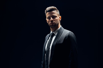 Obraz premium Handsome confident man in black suit on dark background