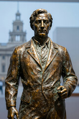 Fototapeta premium Bronze Statue of a Man in Suit Standing Outdoors with City Building Background, Realistic Sculpture for Historical Monument or Public Space Use