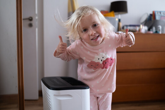 Independent 4 year old girl turning on a modern air dehumidifier to control humidity in her room
