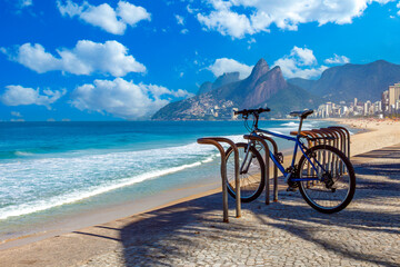 Fototapeta premium Blue mountain bike parked on the Ipanema beach boardwalk with Two Brothers Mountain (Morro Dois Irmãos) and the Atlantic Ocean in the background, Rio de Janeiro, Brazil.