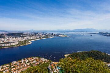 Fototapeta premium High-angle panoramic view of Guanabara Bay featuring Santos Dumont Airport, the Rio-Niteroi Bridge, and the downtown Rio de Janeiro skyline under a clear blue sky.